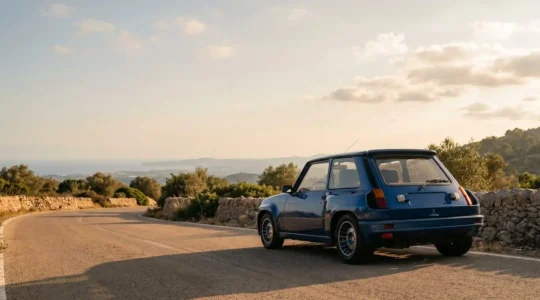 Renault 5 Turbo jaune vue de trois quarts arrière sur une route de montagne sinueuse évoquant le Tour de Corse